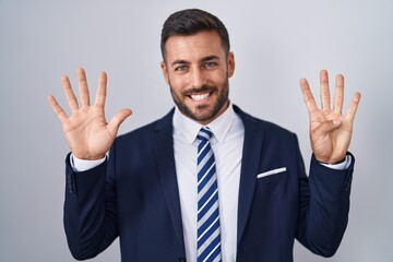 Handsome hispanic man wearing suit and tie showing and pointing up with fingers number nine while smiling confident and happy.