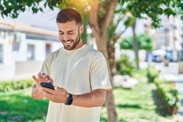 Young hispanic man smiling confident using smartphone at park