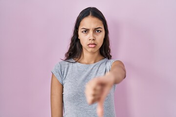 Young brazilian woman wearing casual t shirt over pink background looking unhappy and angry showing rejection and negative with thumbs down gesture. bad expression.