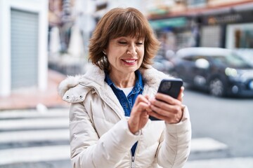 Middle age woman smiling confident using smartphone at street