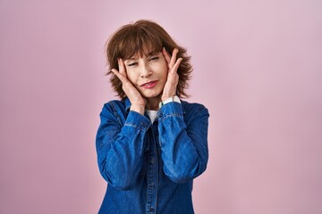 Middle age woman standing over pink background tired hands covering face, depression and sadness, upset and irritated for problem