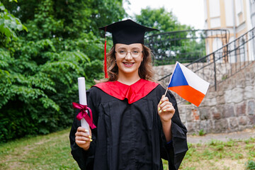 Young czech girl wearing graduation gown and hat holding flag of Czech Republic smiling happy and positive.