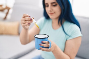 Young caucasian woman pouring liquid on cup sitting on sofa at home