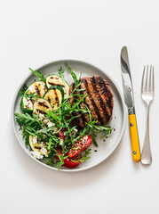 Steak and  vegetable salad with grilled zucchini, tomatoes and arugula on a light background, top view