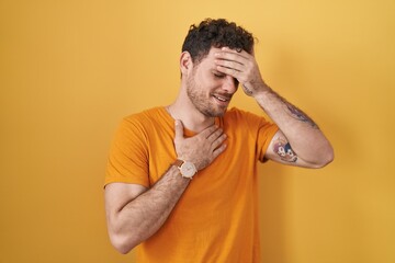 Young hispanic man standing over yellow background touching forehead for illness and fever, flu and cold, virus sick