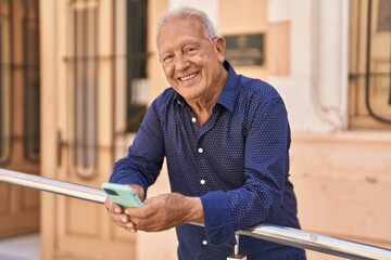 Senior grey-haired man smiling confident using smartphone at street