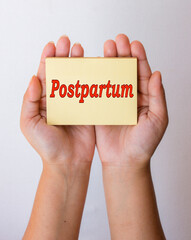 Hand holding Postpartum text word or message on yellow background note paper. Medical and women's...