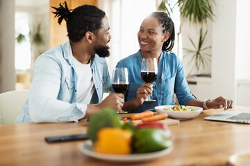 Happy African American couple talking while drinking red wine during lunch time at home