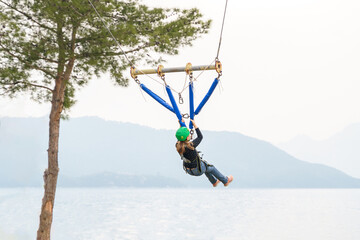 Teenage teen girl bungee flying in rope amusement park. Climbing harness equipment, green sports safety helmet. Hanging obstacle course. Kids children's fear scary high dangerous attraction