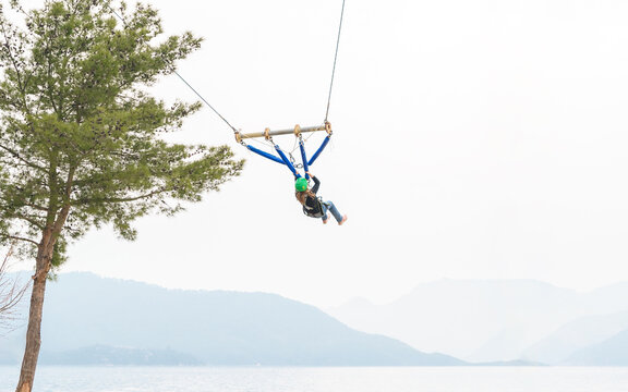 Teenage teen girl bungee flying in rope amusement park. Climbing harness equipment, green sports safety helmet. Hanging obstacle course. Kids children's fear scary high dangerous attraction