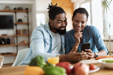 Happy African American couple using a phone while having breakfast in the morning.