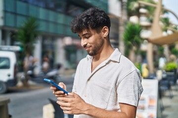 Young arab man smiling confident using smartphone at street