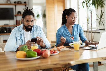 Young African American couple using wireless devices while having breakfast in the morning