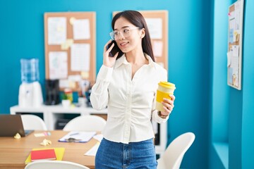 Young chinese woman business worker talking on smartphone drinking coffee at office