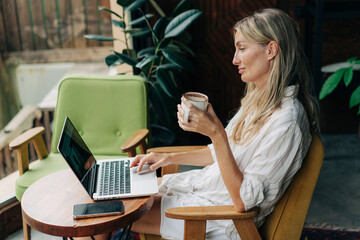 Woman freelancer sitting in coffee house working on laptop.
