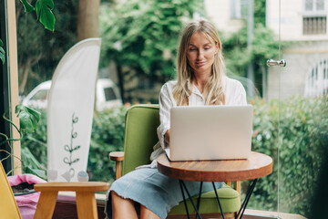 Young woman freelancer works remotely while sitting in a modern coffee shop.