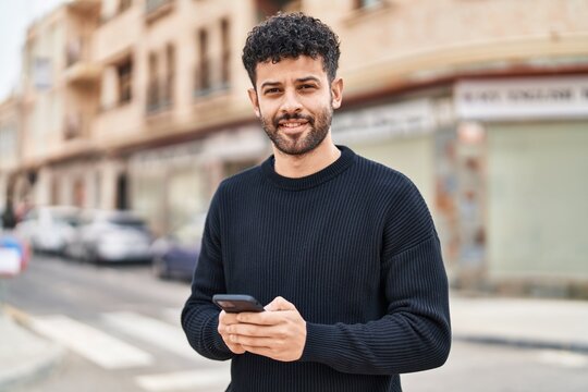Young arab man smiling confident using smartphone at street