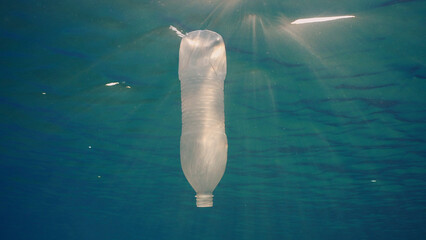 Disposable plastic bottle drift under surface of water in bright sunrays. A plastic bottle is...