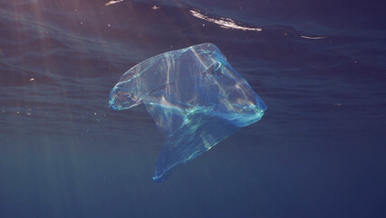 Disposable blue plastic bag floats under surface in blue water in sunrays. Plastic bag thrown into sea drifts under surface of blue water in morning sunlight, Red sea, Egypt