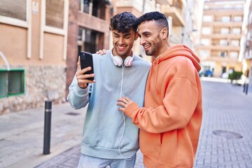 Two man couple hugging each other using smartphone at street