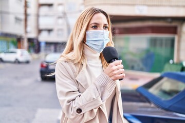 Young blonde woman reporter wearing medical mask working at street