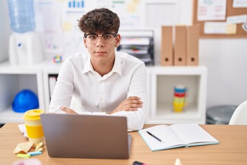 Young hispanic teenager business worker smiling confident sitting with arms crossed gesture at office