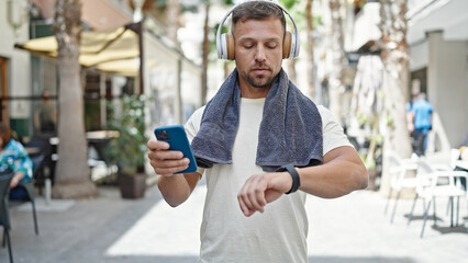 Young man wearing sportswear listening to music using smartphone and smartwatch at street
