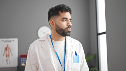 Young hispanic man doctor looking to the side with serious expression at clinic