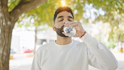 Young hispanic man drinking water at park