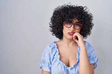 Young brunette woman with curly hair wearing glasses over isolated background thinking looking tired and bored with depression problems with crossed arms.