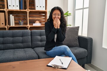 Young asian woman at consultation office laughing and embarrassed giggle covering mouth with hands, gossip and scandal concept