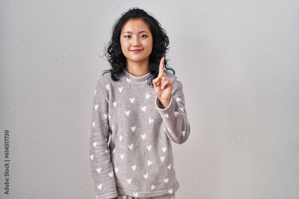 Sticker young asian woman wearing pajama showing and pointing up with finger number one while smiling confid