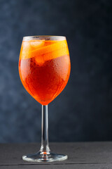 Aperol Spritz cocktail on dark wooden planks. Cocktail Aperol Spritz with oranges and ice cubes in glass. Traditional italian aperitif cocktail