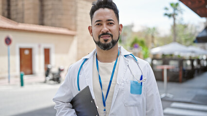 Young latin man doctor smiling confident holding medical report at coffee shop terrace