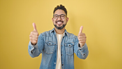 Naklejka premium Young latin man smiling with thumbs up over isolated yellow background