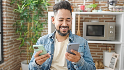 Young latin man using smartphones sitting on table at dinning room