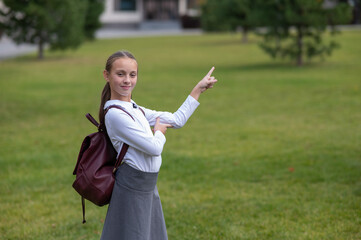 Caucasian girl in uniform and with a backpack points to an empty place outdoors after school.