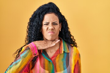 Middle age hispanic woman standing over yellow background cutting throat with hand as knife, threaten aggression with furious violence