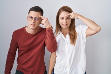 Mother and son standing together over isolated background pointing unhappy to pimple on forehead, ugly infection of blackhead. acne and skin problem
