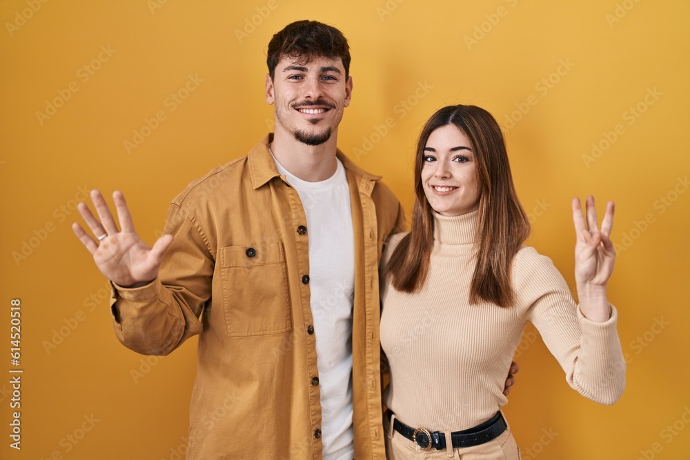 Poster Young hispanic couple standing over yellow background showing and pointing up with fingers number eight while smiling confident and happy.