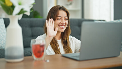 Young beautiful hispanic woman having video call sitting on floor at home