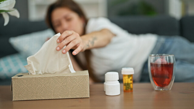 Young beautiful hispanic woman lying on the sofa sick using tissue at home