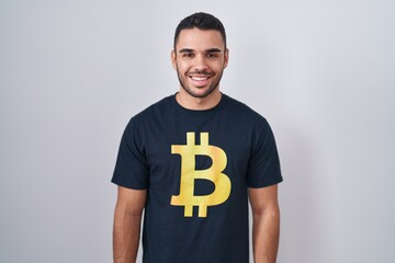 Young hispanic man wearing bitcoin t shirt with a happy and cool smile on face. lucky person.