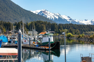 fishing boats moored in the docks in Sitka Alaska with scenic snowcapped mountains in the background  - obrazy, fototapety, plakaty