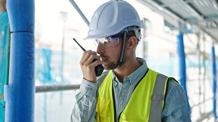 Fototapeta na wymiar Young caucasian man architect talking on walkie-talkie at construction place
