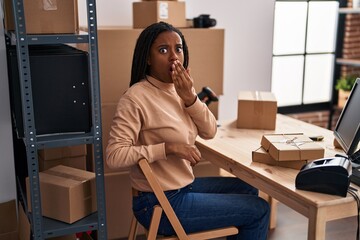 Young african american with braids working at small business ecommerce covering mouth with hand,...