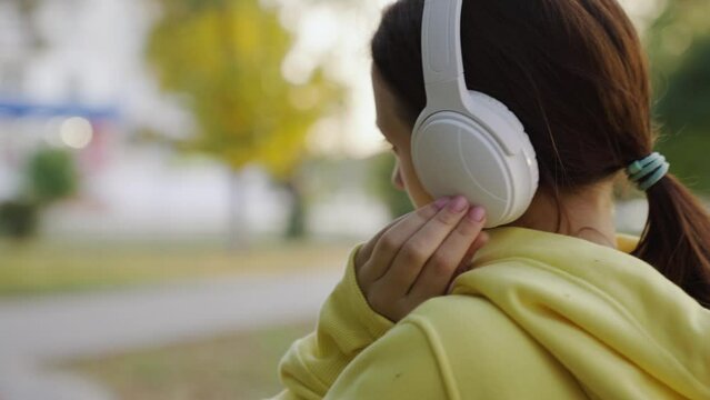 Young active woman walks outdoors in music headphones, listens to audiobooks, has rest. Girl goes to park listens to music on headphones. Fashionable girl walks along city street, Weekend. Life style