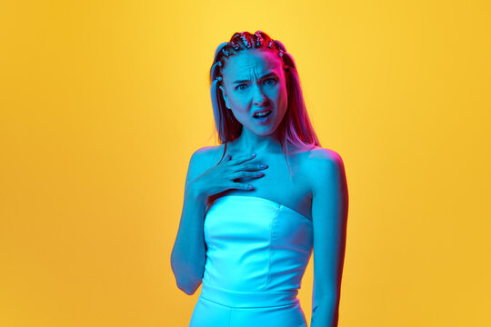 What. Portrait of young native girl with cute hairstyle posing with face of misunderstanding against yellow studio background in neon light. Concept of youth, emotions, beauty, lifestyle, ad