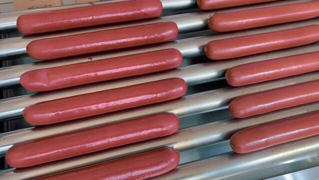 Many hot dog sausages are fried on a rotating electric grill.