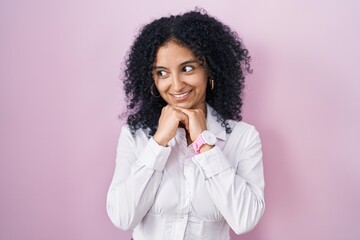 Hispanic woman with curly hair standing over pink background laughing nervous and excited with...